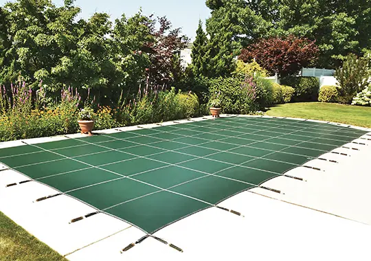Professionally fitted blue safety cover secured over an inground pool in a landscaped backyard.