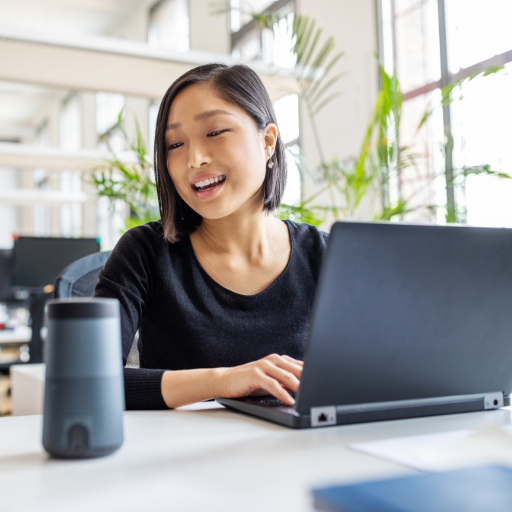 Woman smiling at her laptop in a bright modern office with a smart speaker in the foreground, looking energized and productive Woman smiling at her laptop in a bright modern office with a smart speaker in the foreground, looking energized and productive