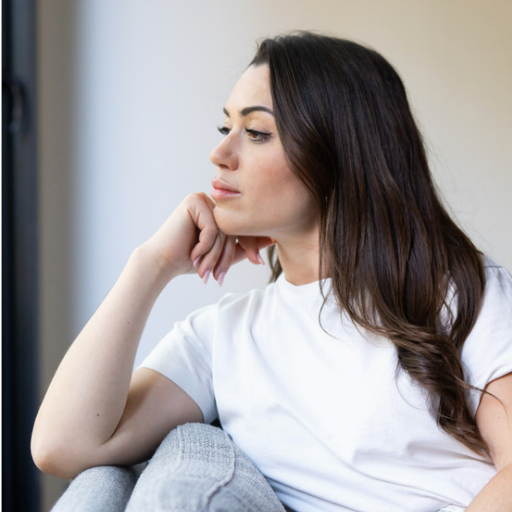 Woman resting her chin on her hand while looking thoughtfully out a window.