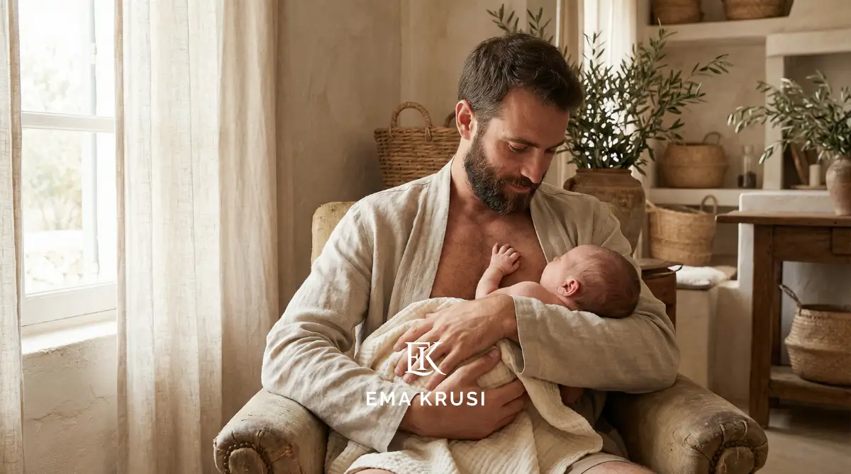 Père assis dans un fauteuil tenant un nouveau-né contre lui, dans un intérieur chaleureux aux tons naturels.