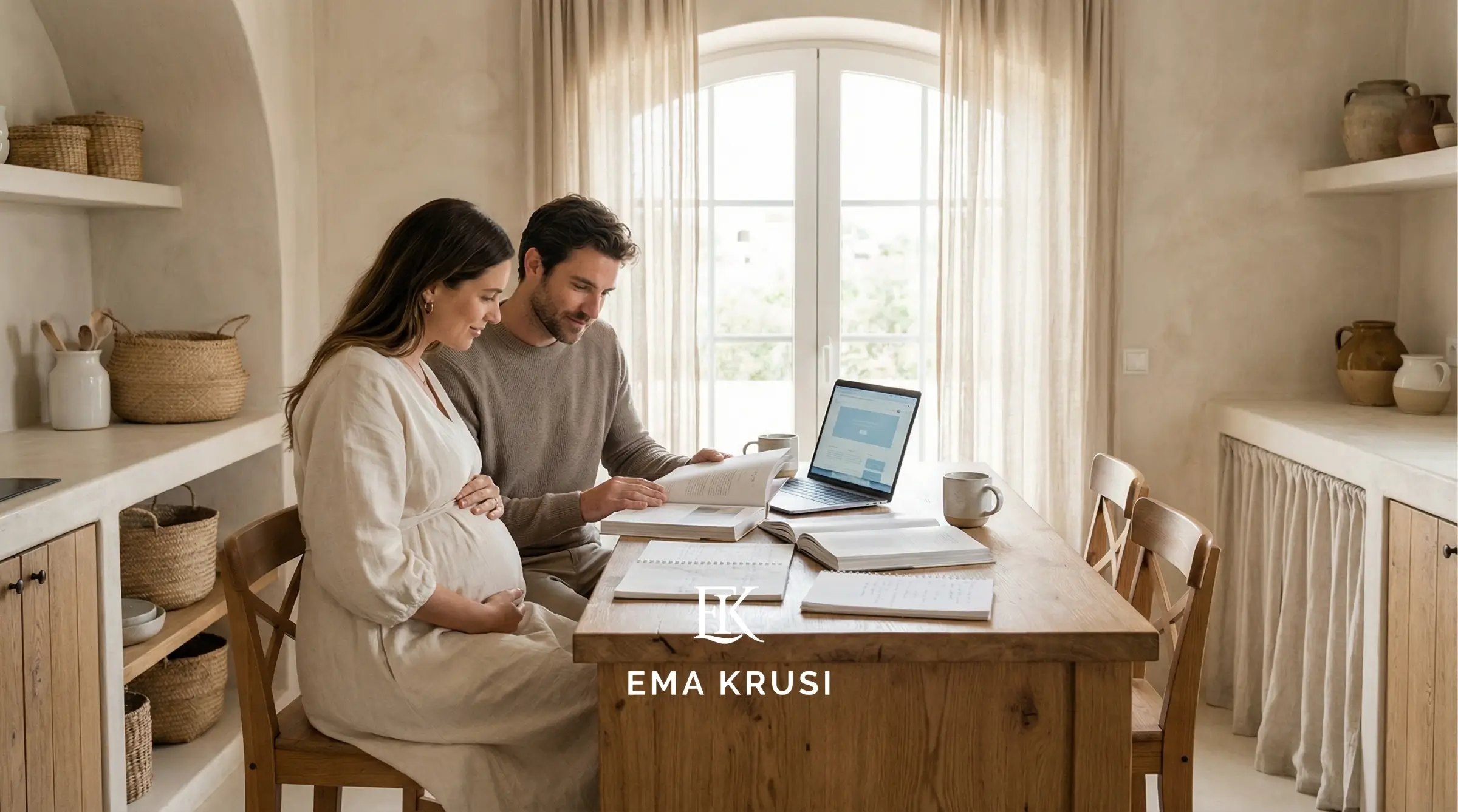 Couple attendant un bébé étudiant des documents à table avec un ordinateur portable, dans une cuisine lumineuse.