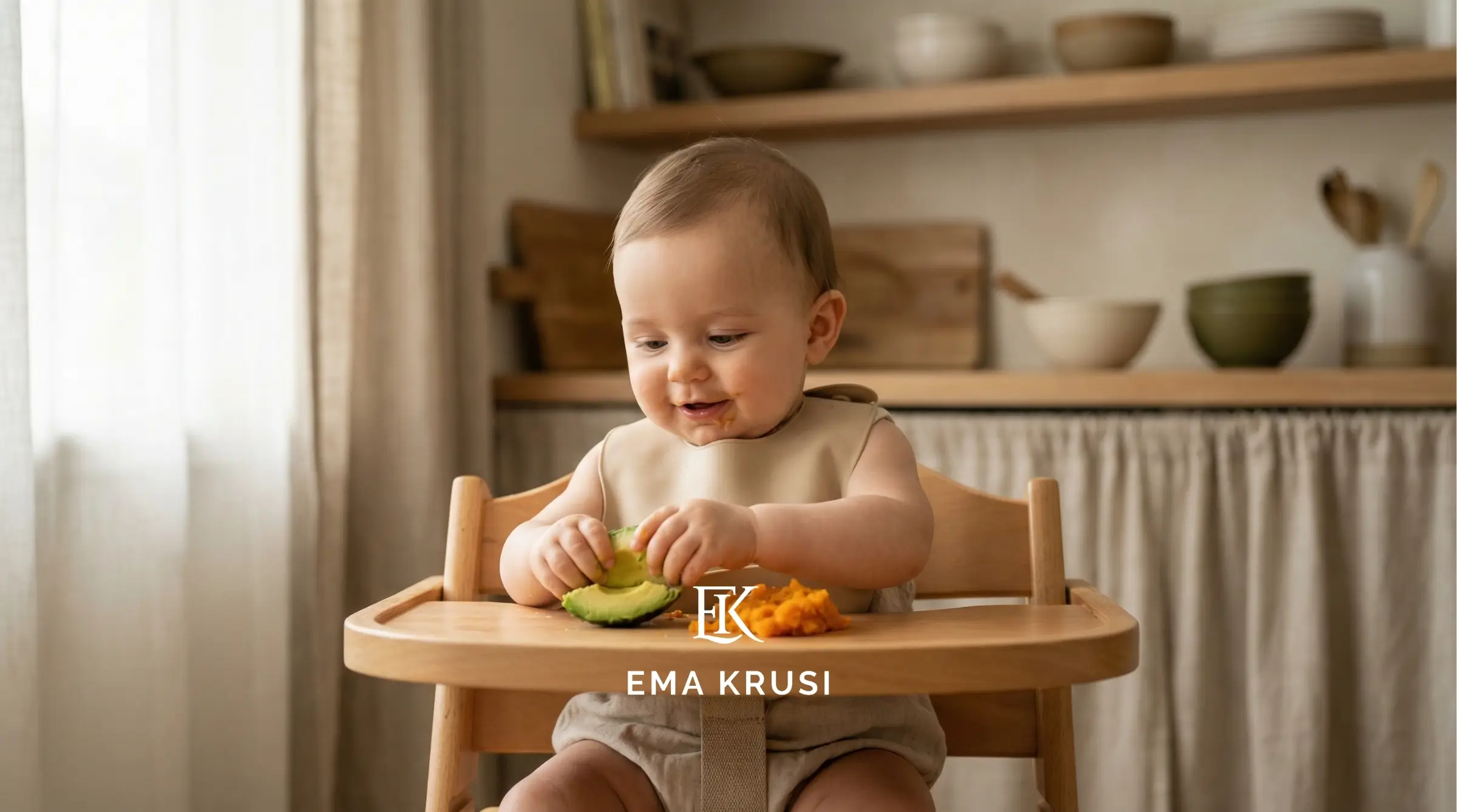 Bébé assis dans une chaise haute mangeant des morceaux d’avocat et de purée, dans une cuisine lumineuse.