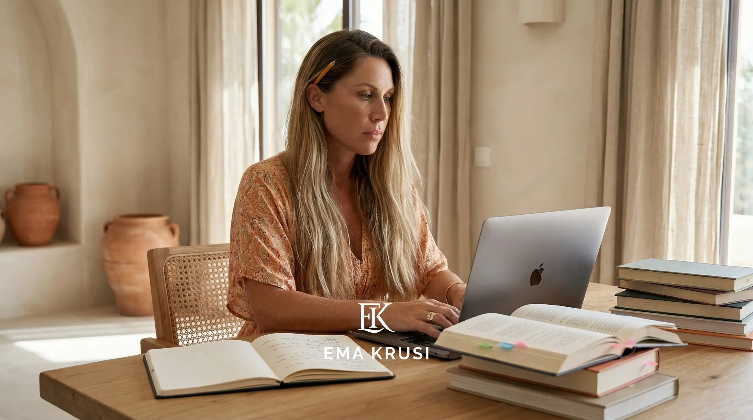 Femme travaillant sur un ordinateur portable avec livres et cahiers ouverts, dans un intérieur aux tons naturels.