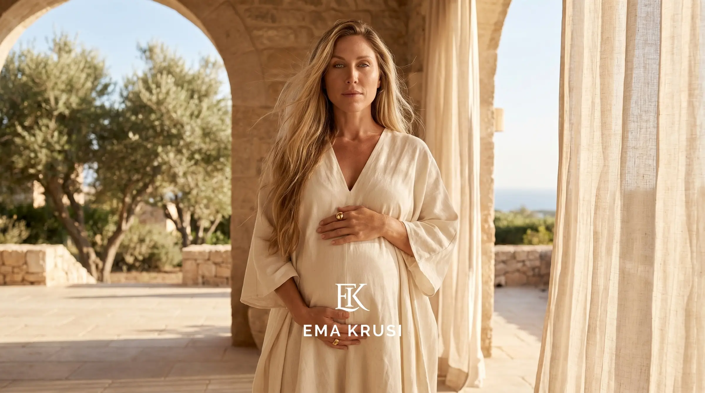 Ema Krusi enceinte, debout dans une maison en pierre baignée de lumière naturelle en Algarve, représentant la sérénité, la confiance et le lien avec son bébé pendant la grossesse.