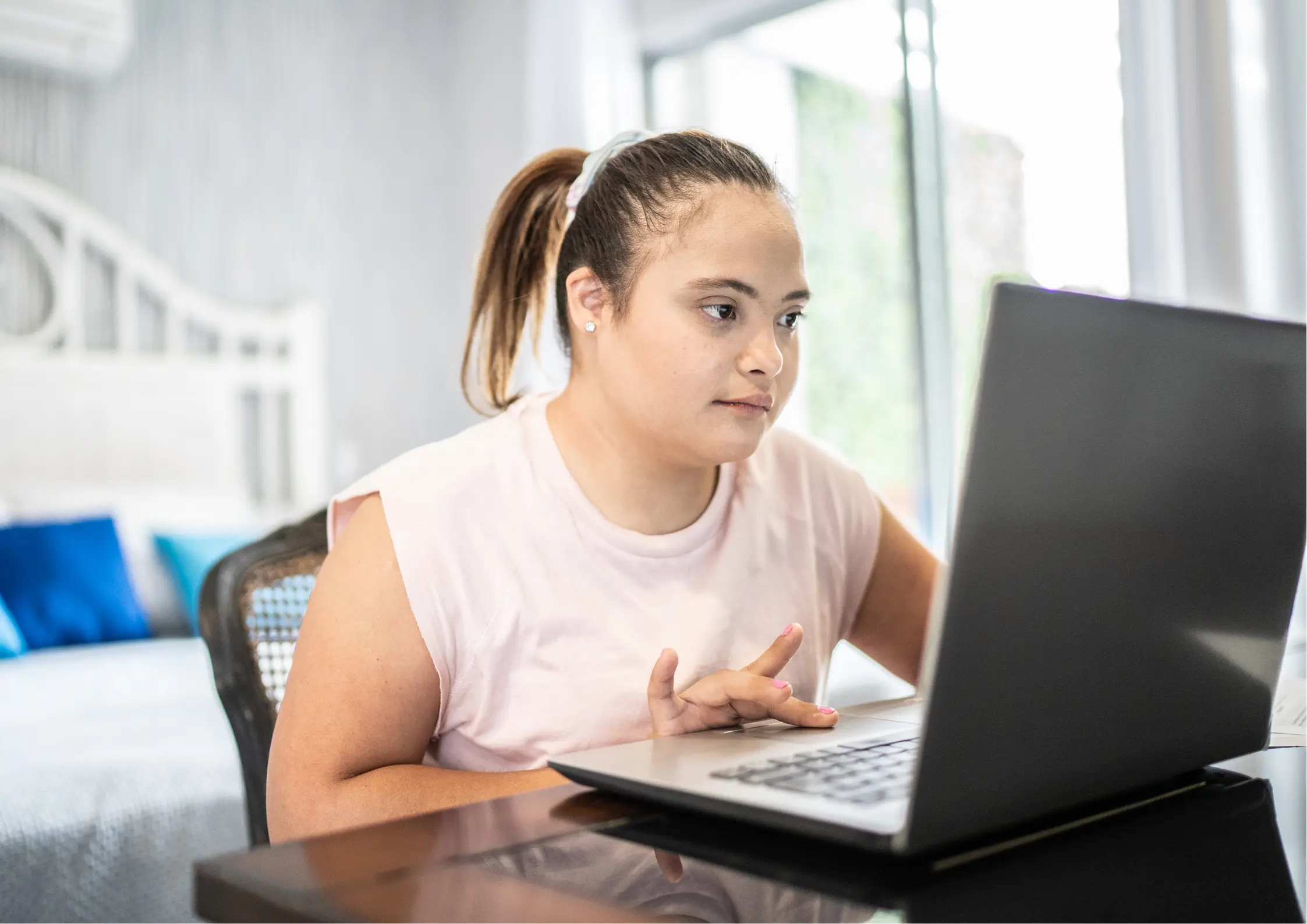 A young woman with Down syndrome focused on her work while using a laptop computer at a desk, representing digital literacy and vocational training for young adults with disabilities.