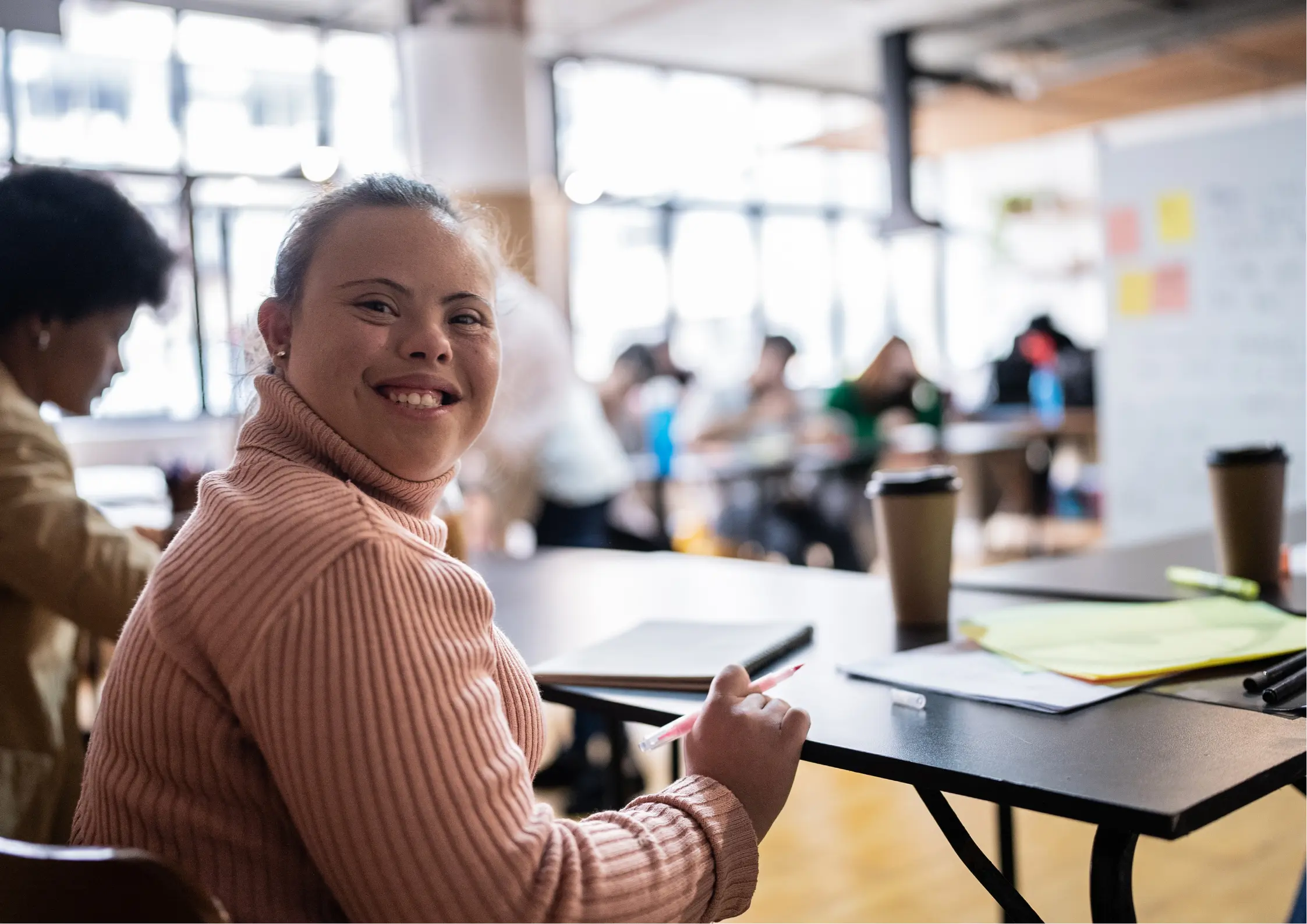 A happy woman with Down syndrome smiling while actively participating in a collaborative office workshop or training session.