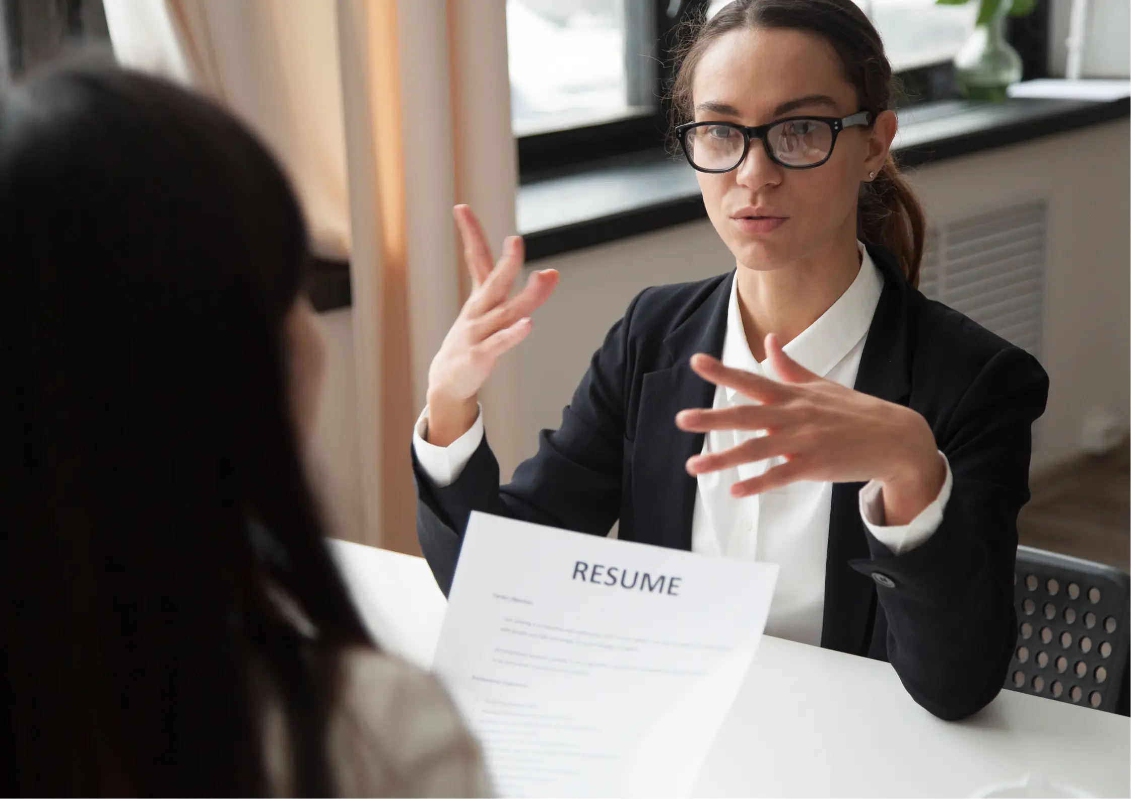 Female interviewer conducting job interview with job candidate, reviewing resume and discussing qualifications in professional office setting, demonstrating interview process and employer communication Female interviewer conducting job interview with job candidate, reviewing resume and discussing qualifications in professional office setting, demonstrating interview process and employer communication
