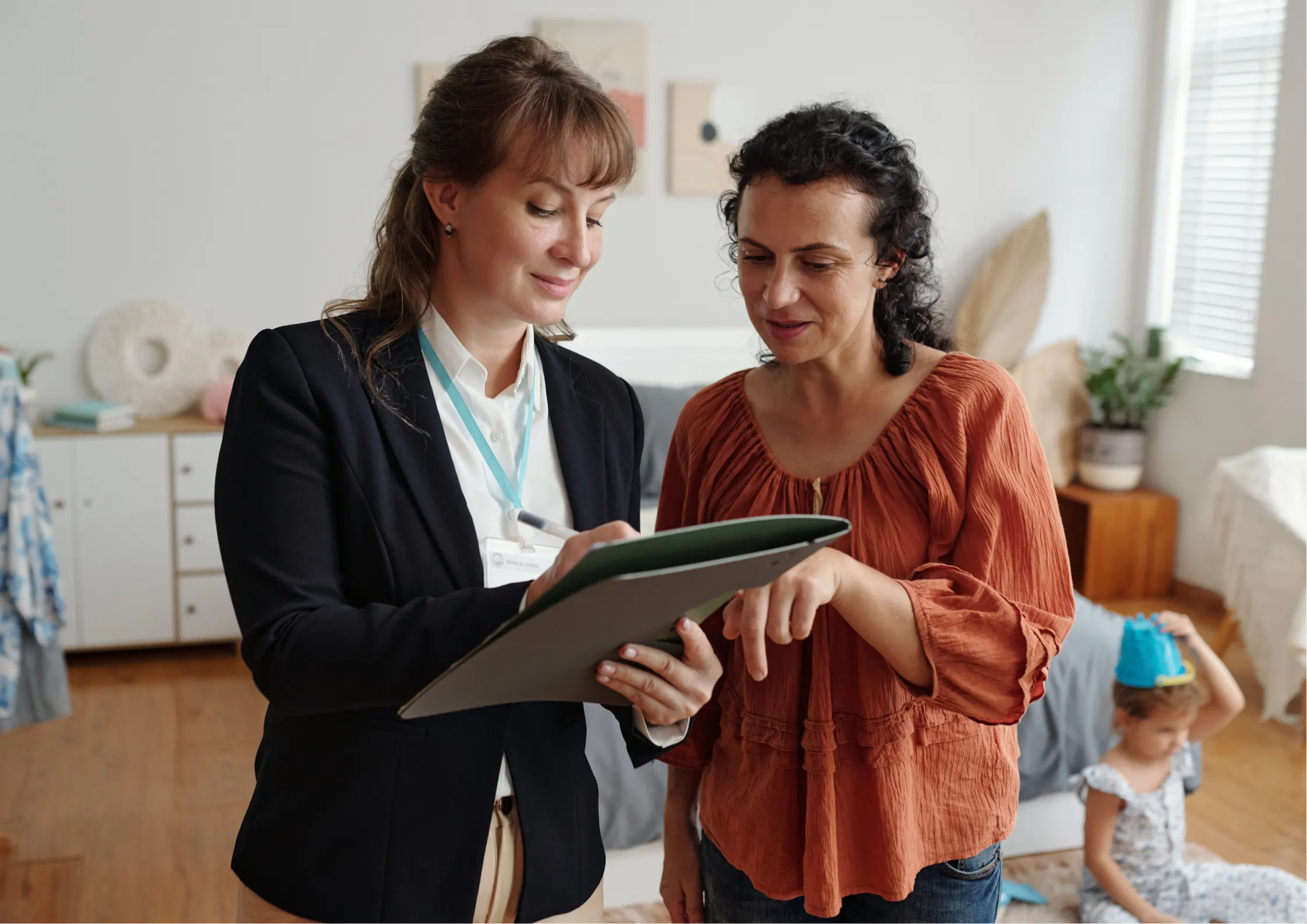 A female education advocate holding a clipboard and reviewing IEP service documents with a mother at home.