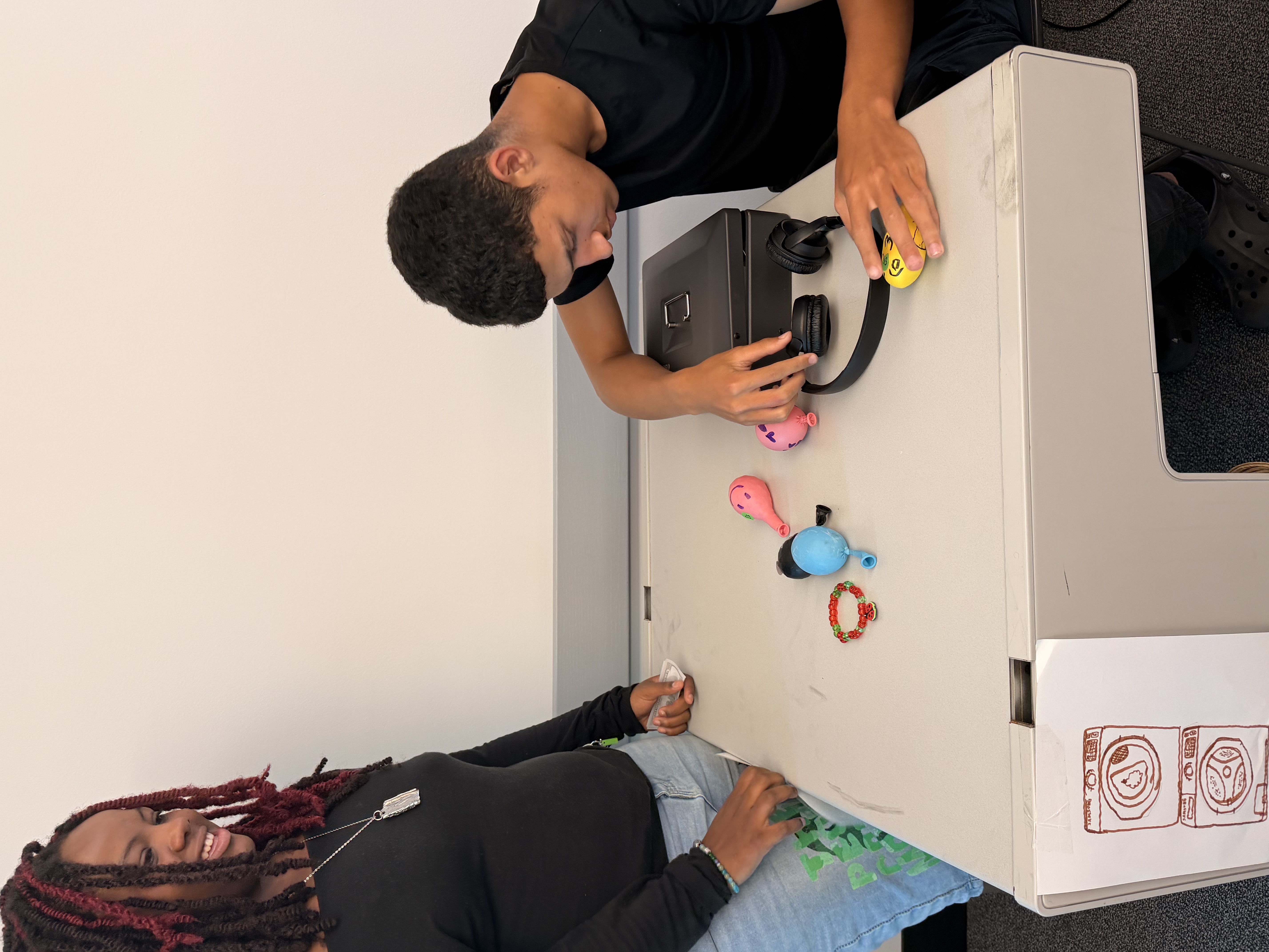 A young man practicing independent living skills at a desk with an instructor observing at Better Steps Life Skills Center.
