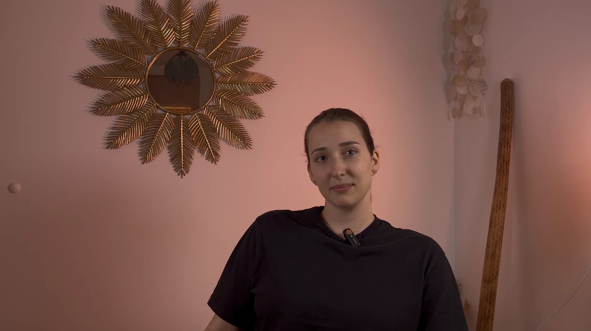 Nő portréja rózsaszín háttér előtt, napsugár formájú fali tükörrel