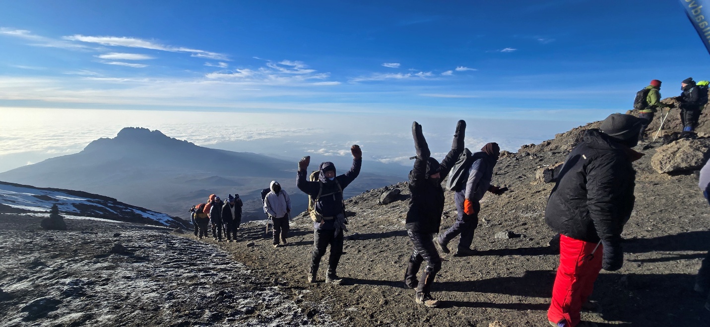 An Inspedition group celebrating on Kilimanjaro above the clouds, with Mawenzi peak in the distance