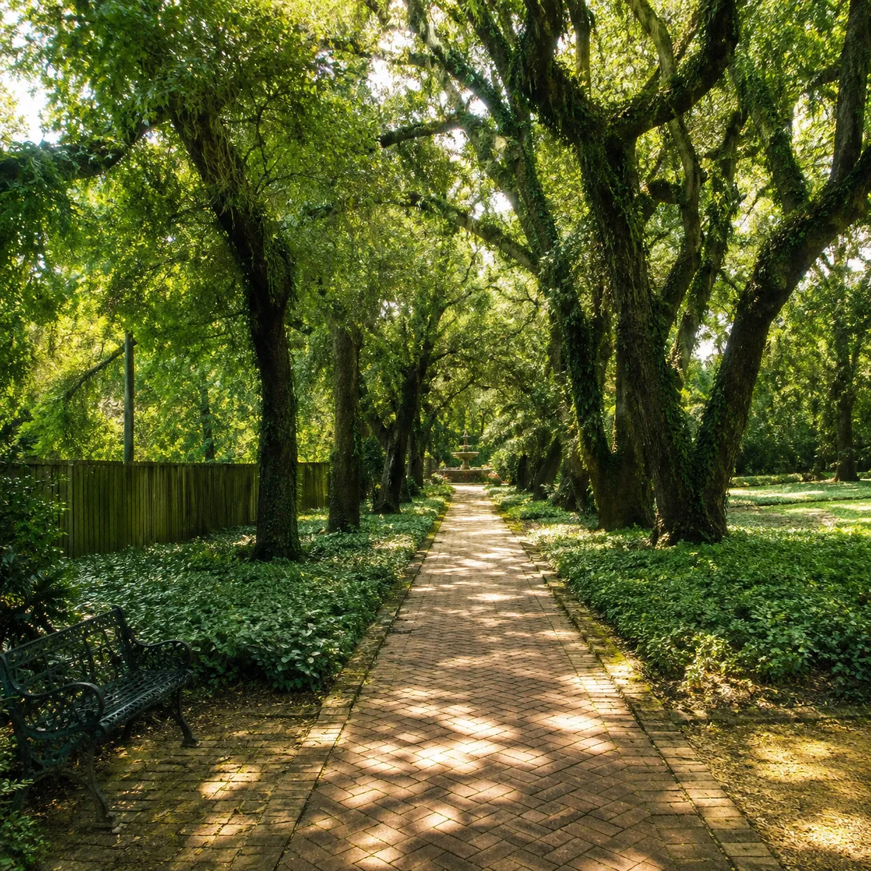 Brick path under mossy live oaks at Hopelands Gardens, a quiet fountain in view.