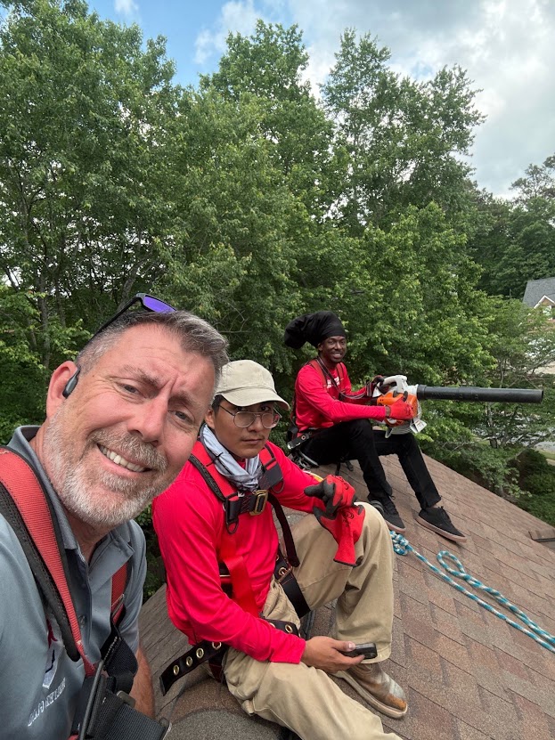 James Scuka on a roof with two Shelter Guard gutter technicians in branded shirts and safety harnesses