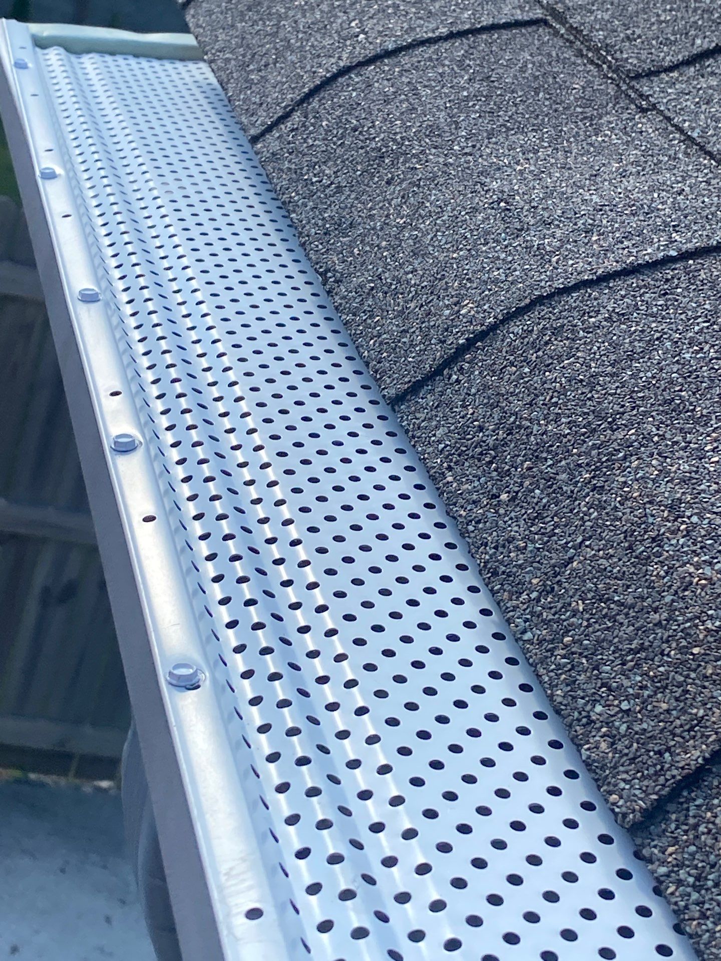 Close view of a silver perforated gutter guard showing the punch pattern and fasteners