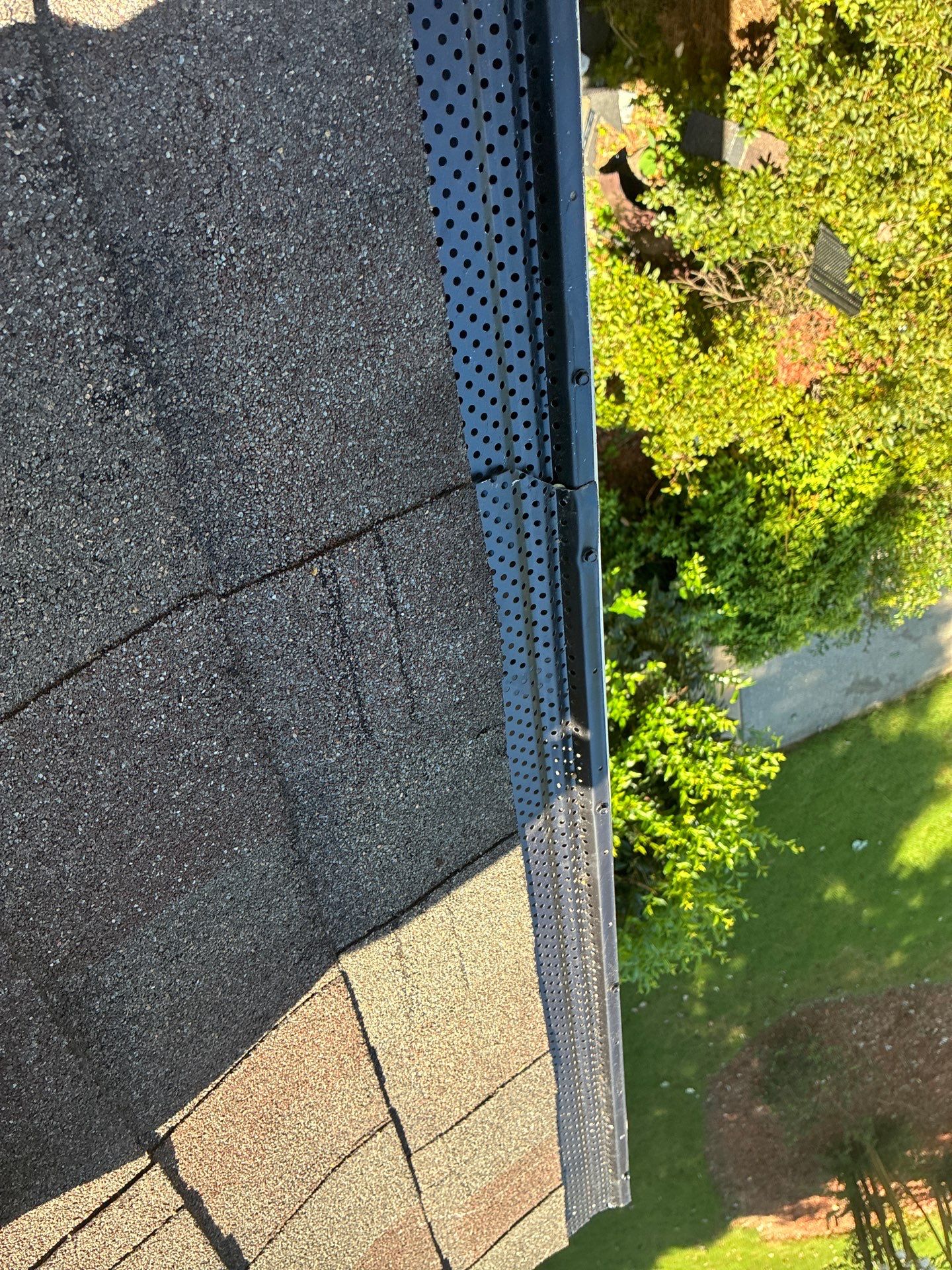 Two different gutter guard styles butted together along the same run, black perforated and silver perforated