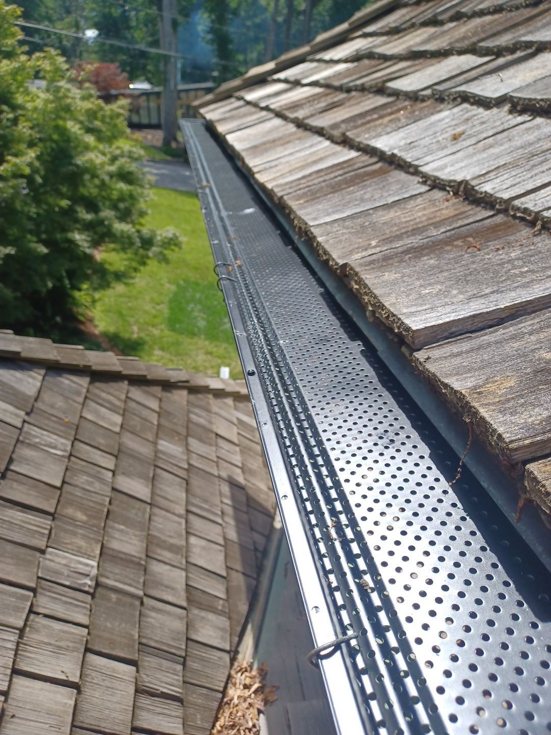Black perforated gutter guard installed along the eave of a wood shake roof