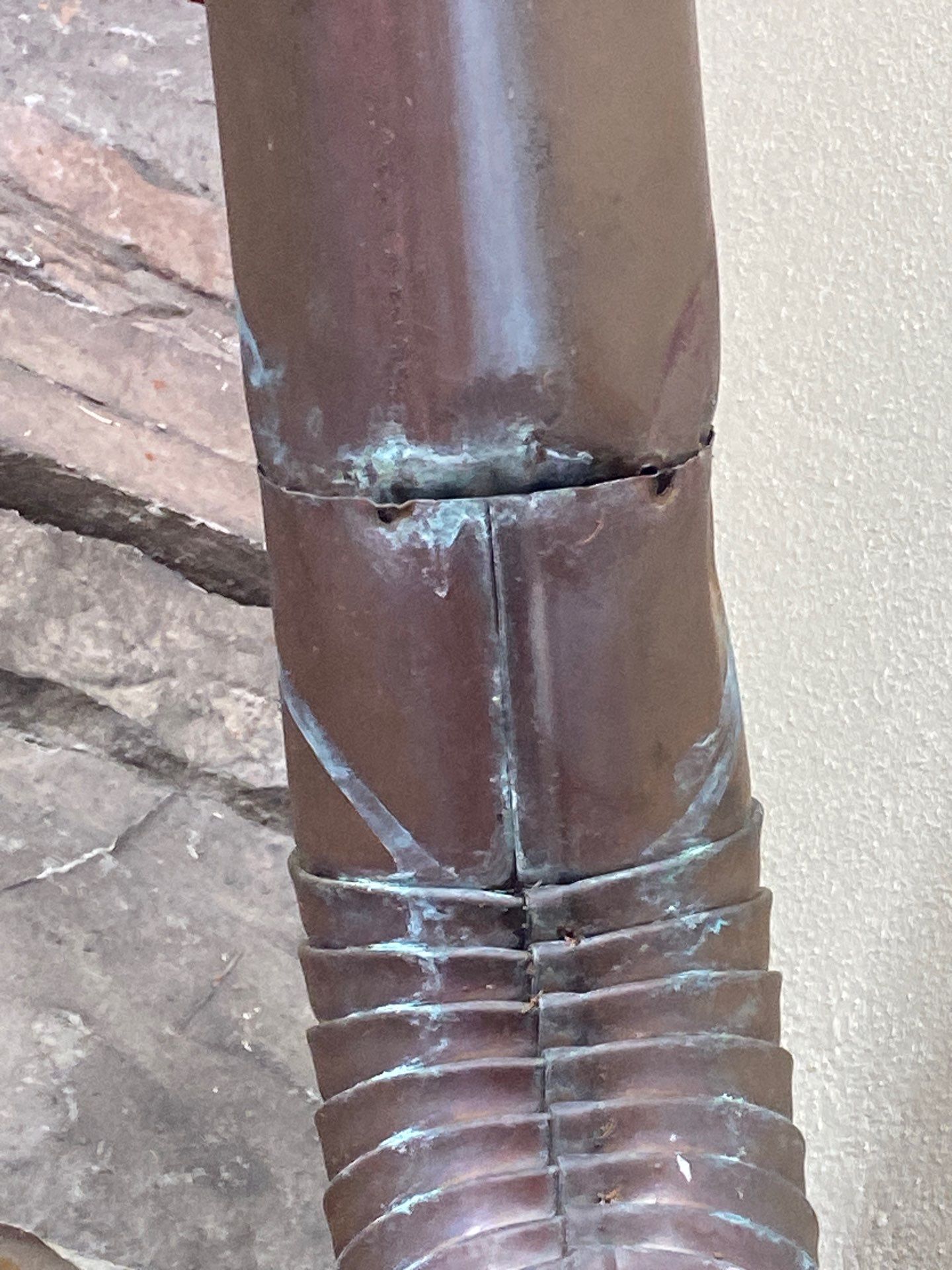 Corroded downspout seam showing green oxidation where the sections join