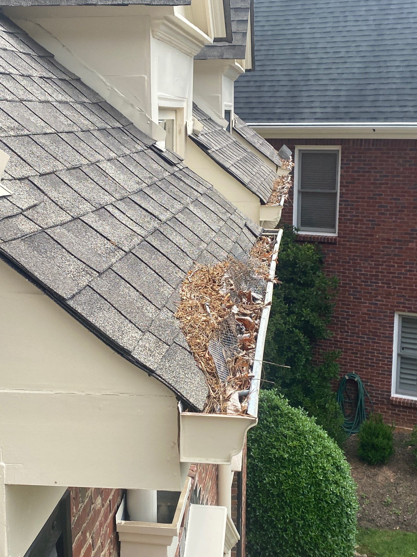 Gutter packed with leaf debris at a roof corner beside a brick wall