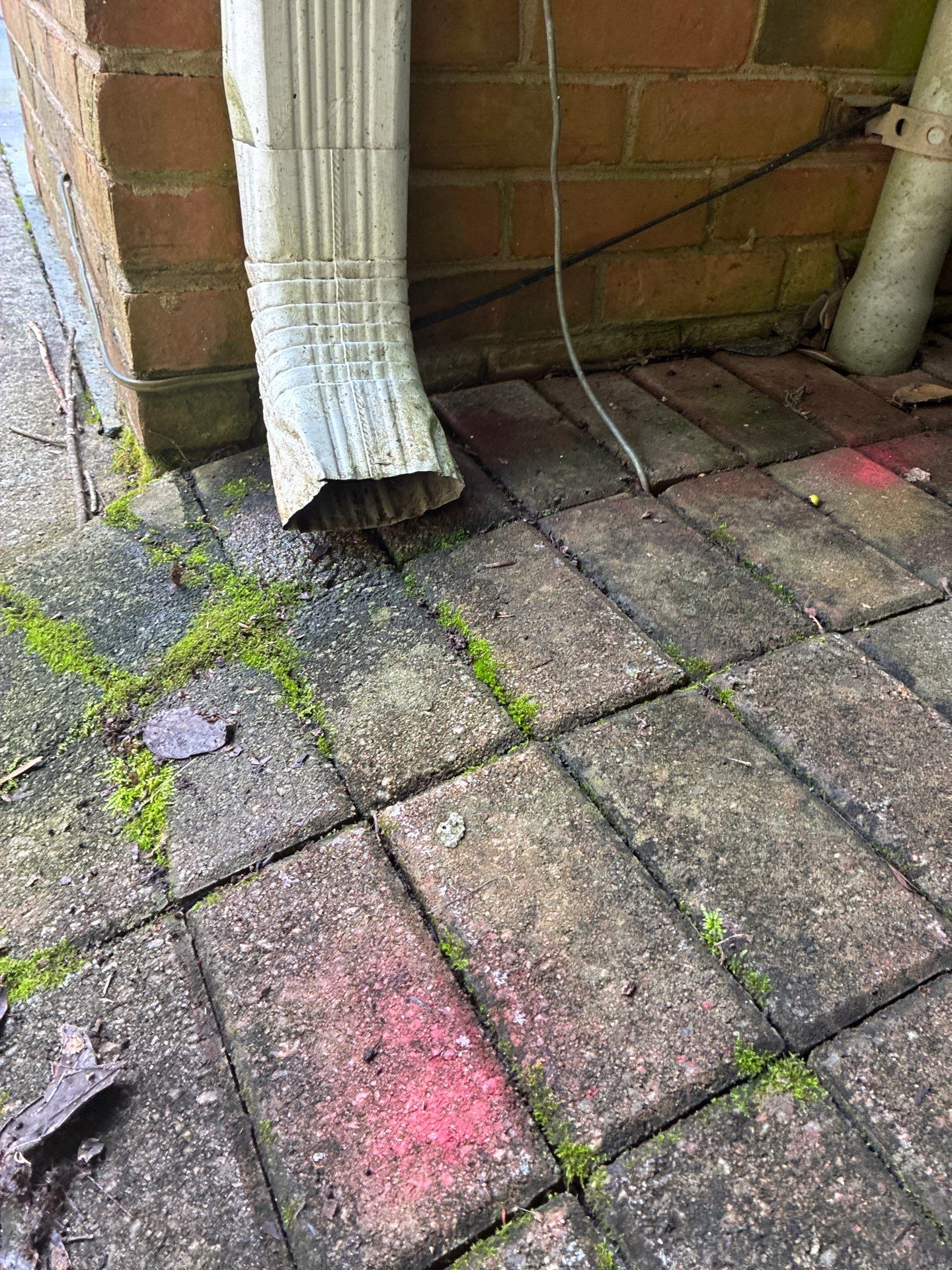 Downspout elbow crushed and disconnected at the base of a brick wall