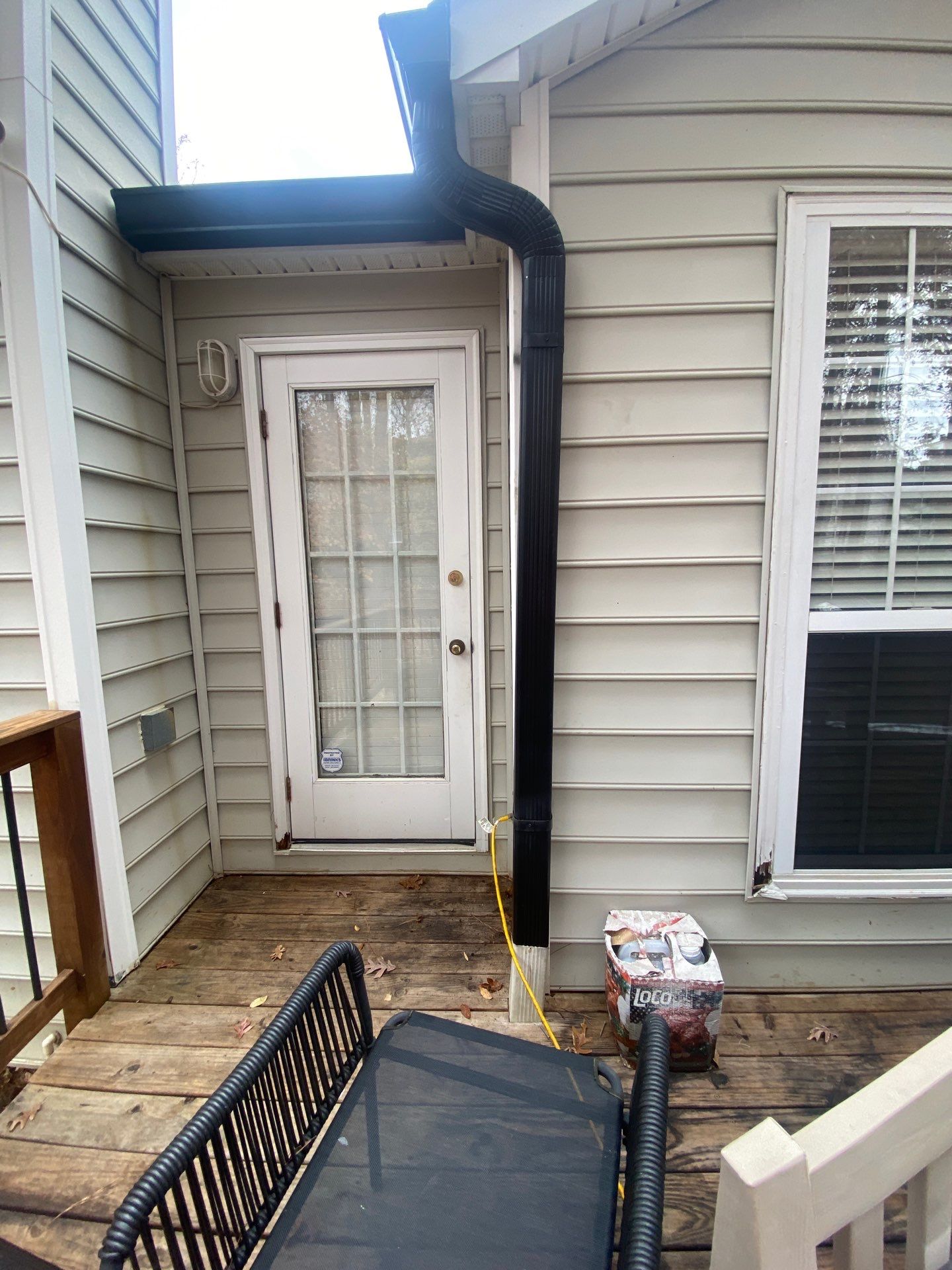 Close-up of a downspout elbow joint running down the corner of a house near a back door