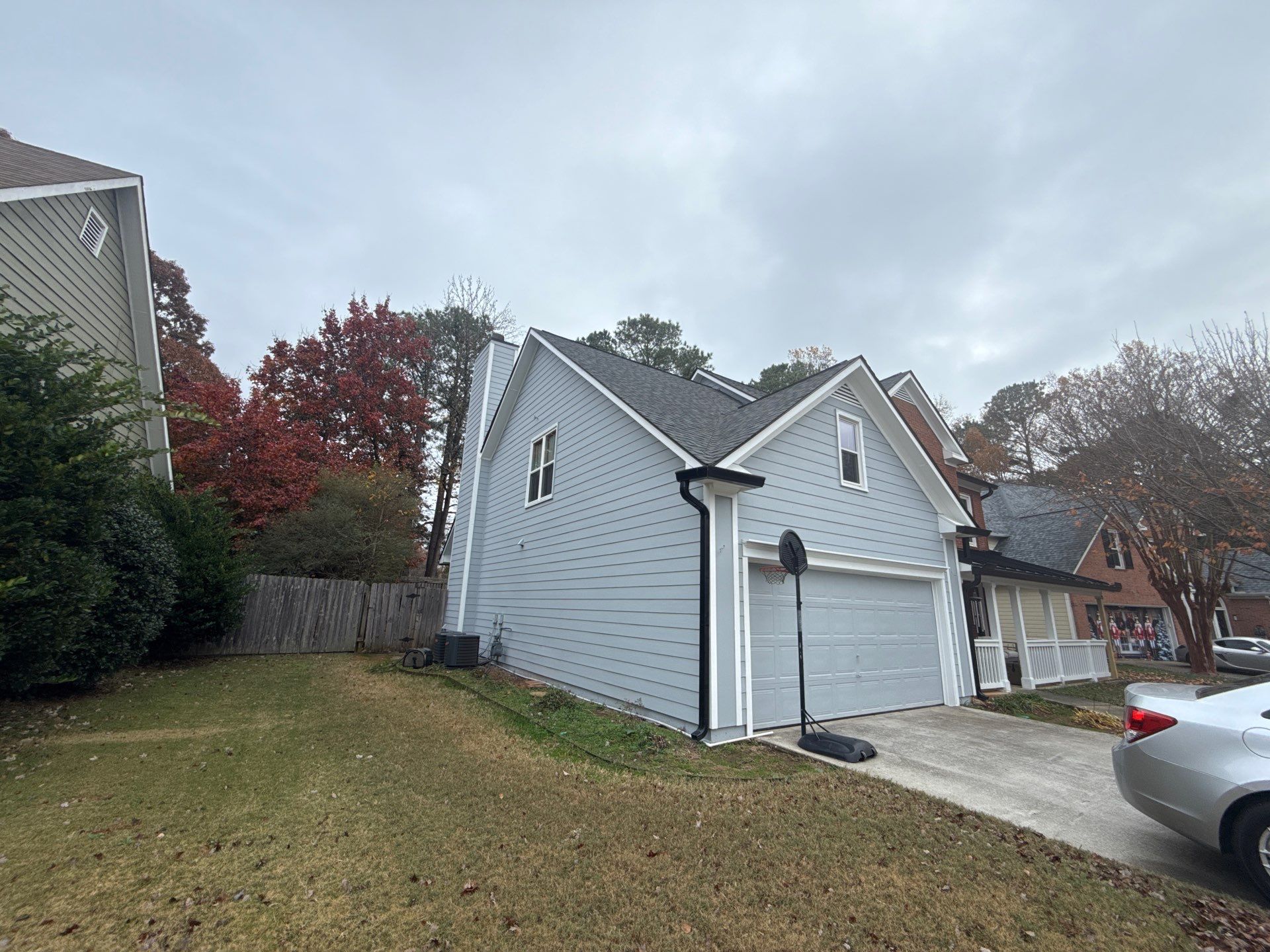 Two-story home exterior with a downspout running down the corner, fall foliage in the background