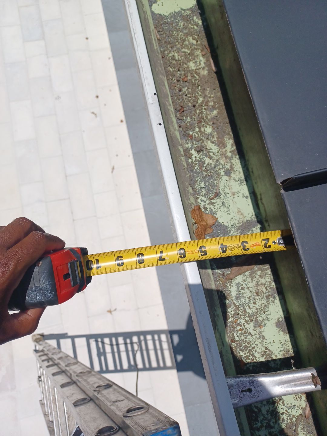Tape measure held against a rusted gutter and fascia