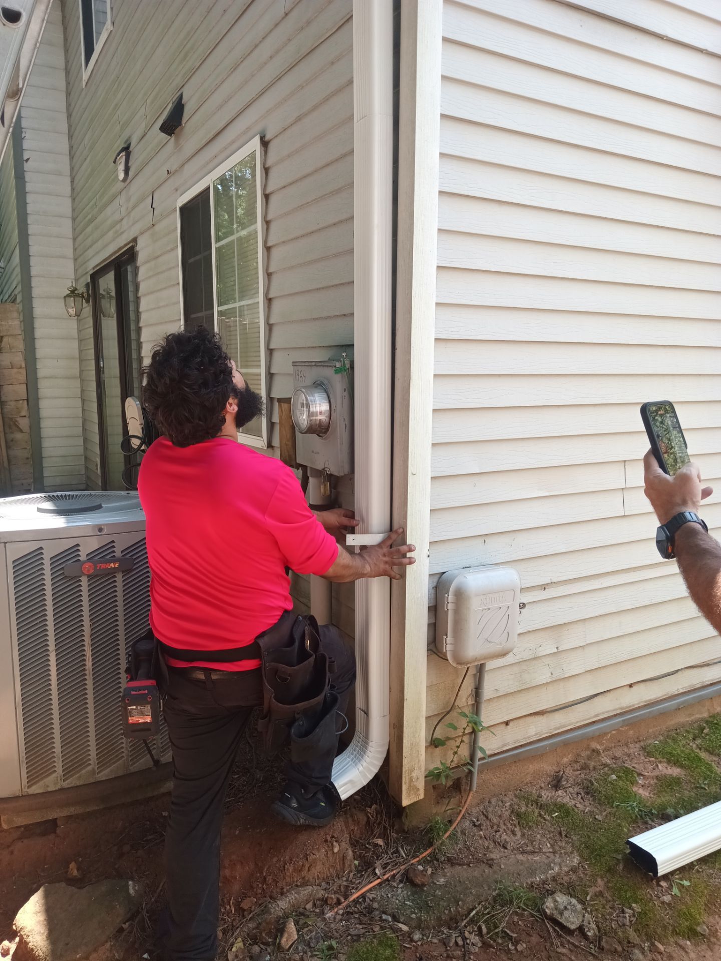 Shelter Guard crew member in a red shirt working on a downspout against siding