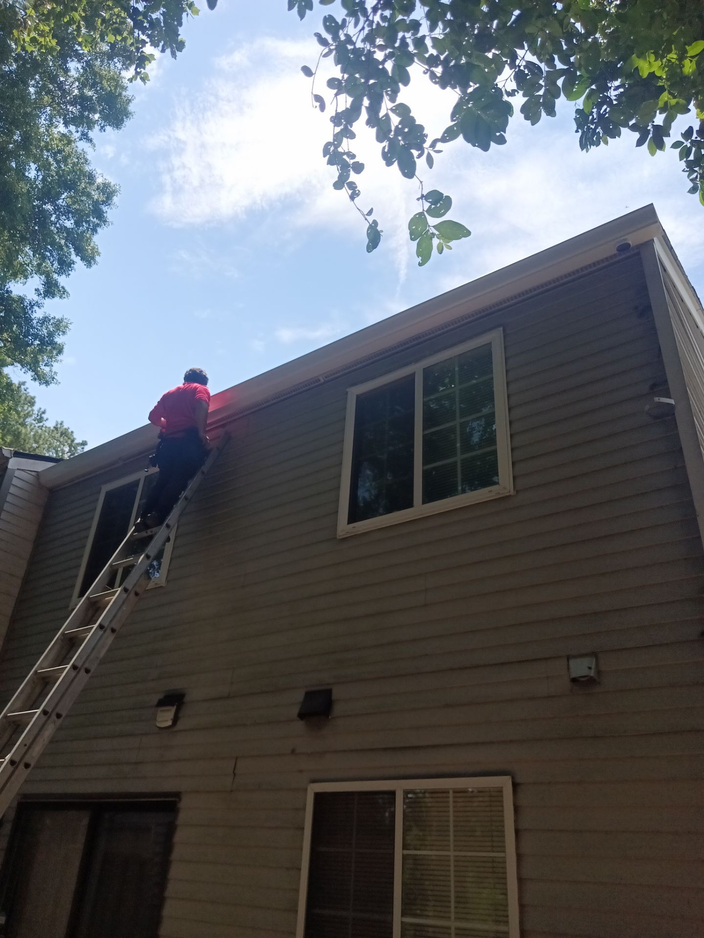 Crew member on a ladder at the roofline of a two-story home