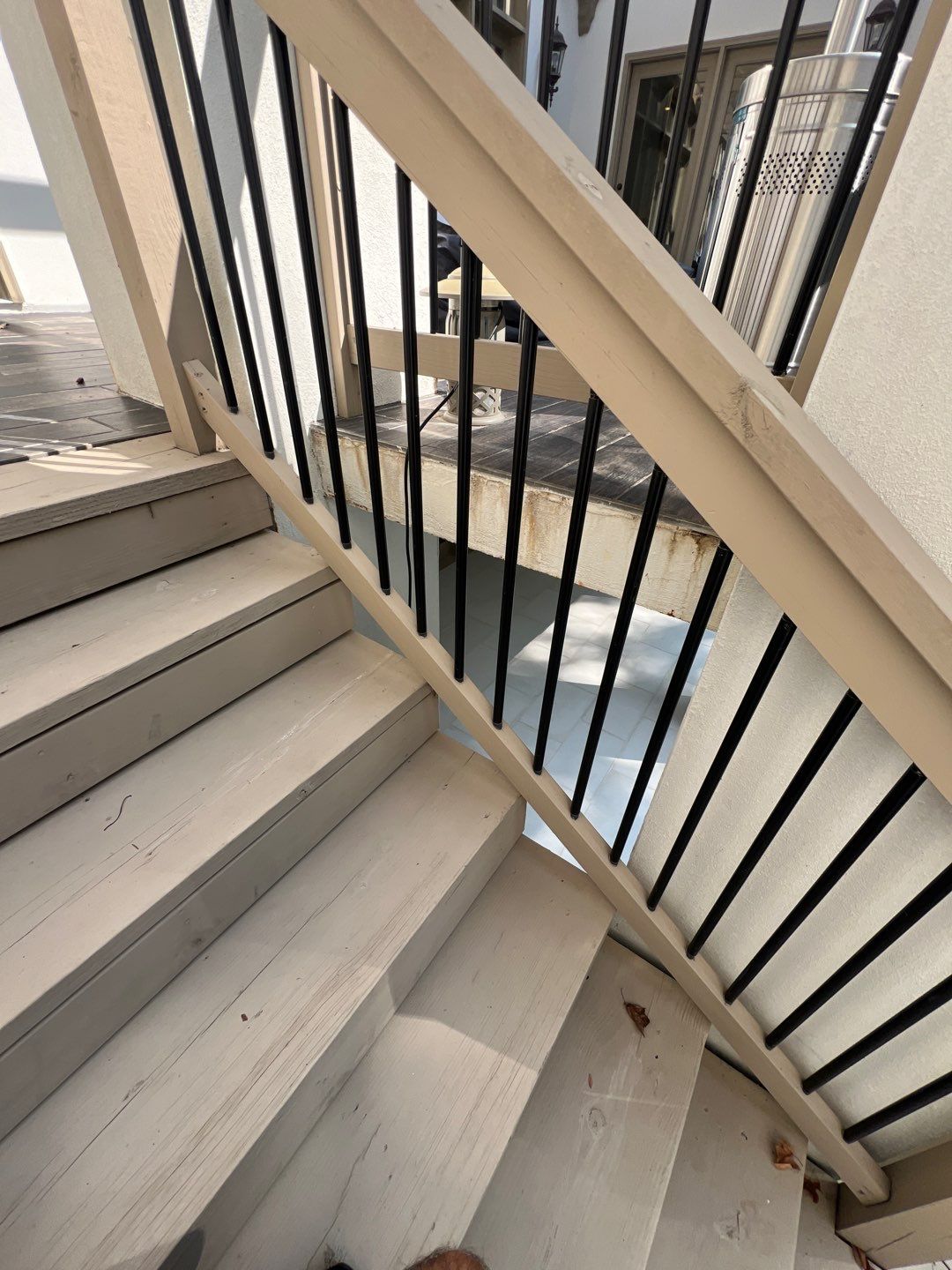 Wooden stairs with a black railing alongside a house