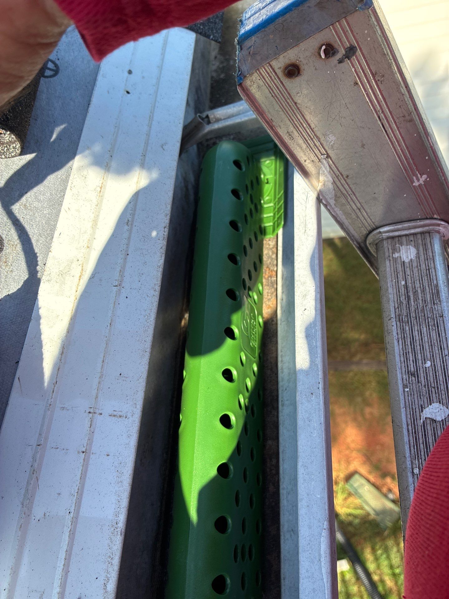 Green gutter guard insert inside a gutter beside a ladder