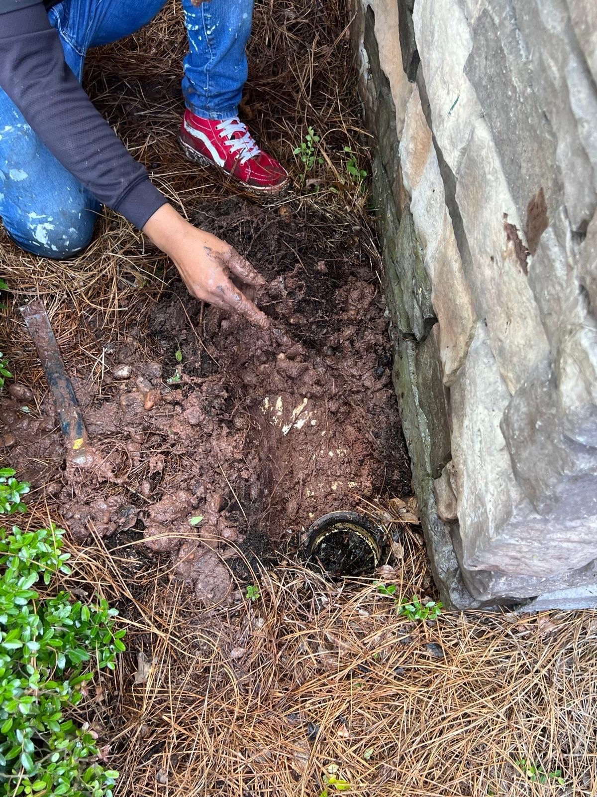 Crew member digging out a drain outlet beside a stone wall