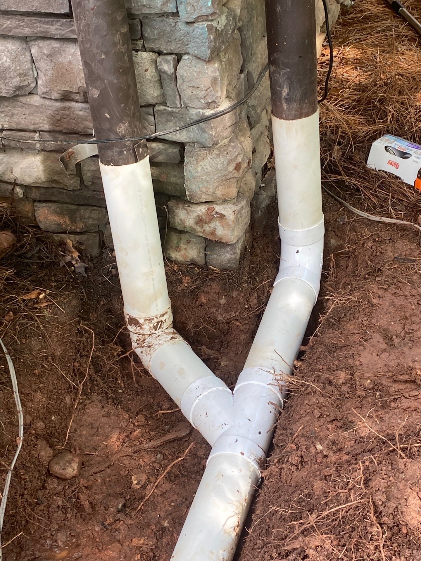 White PVC drain lines tied in at the stone wall