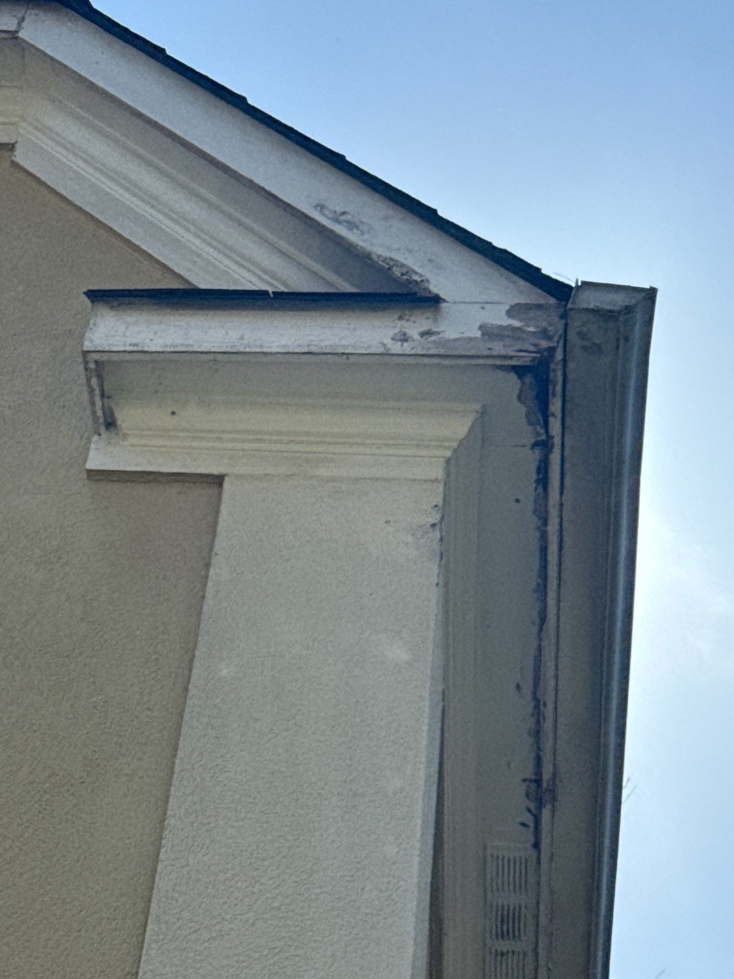 White gutter corner against a stucco wall and blue sky