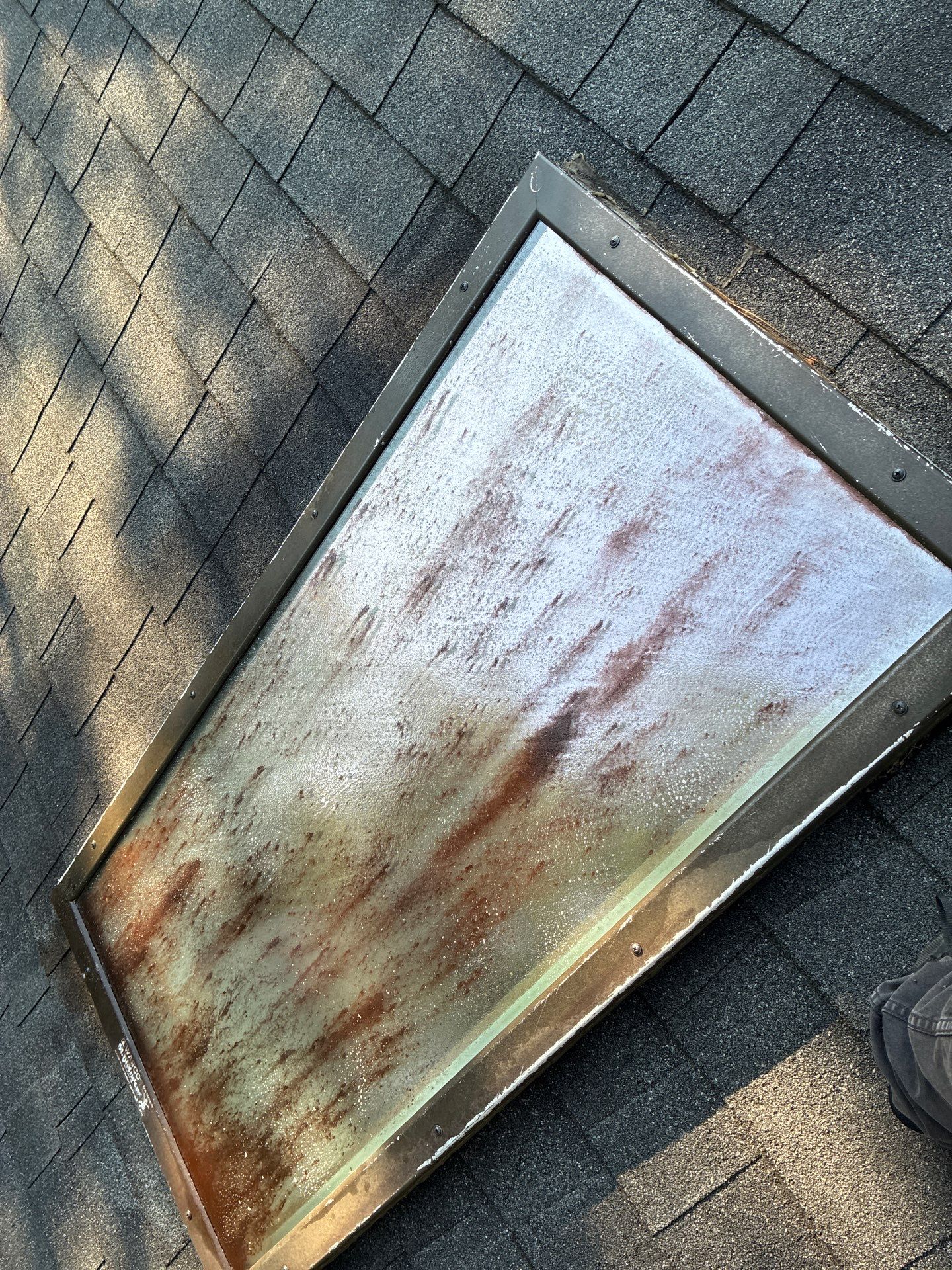 Skylight glass covered in dirt, rust streaks and mineral buildup, exterior view