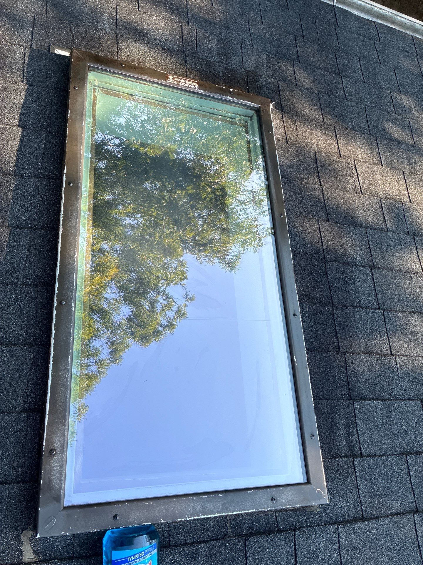 Clean skylight exterior on a shingle roof with trees reflected in the glass