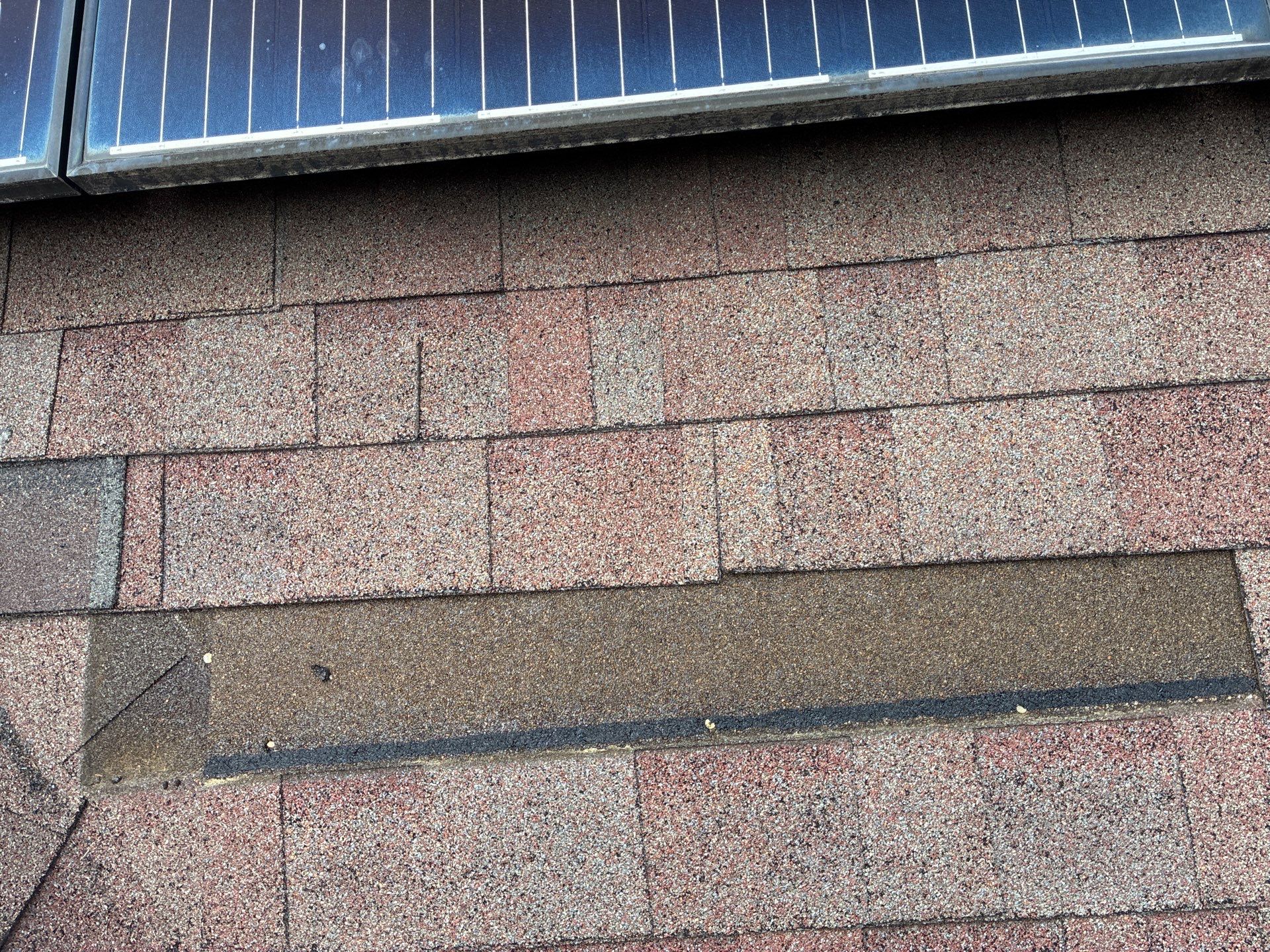 Close-up of worn and patched asphalt shingles near a roof-mounted solar panel