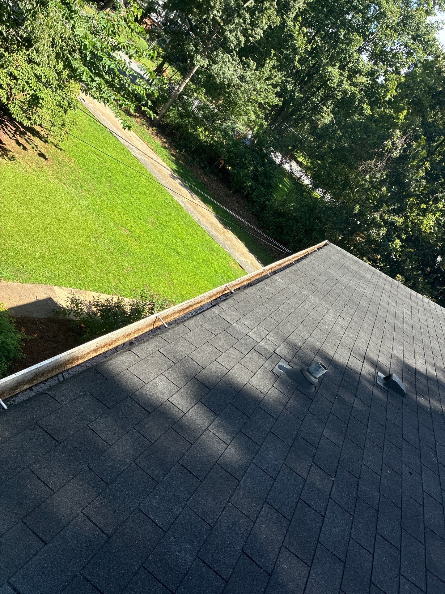 View down a shingle roof edge toward a lawn and tree line