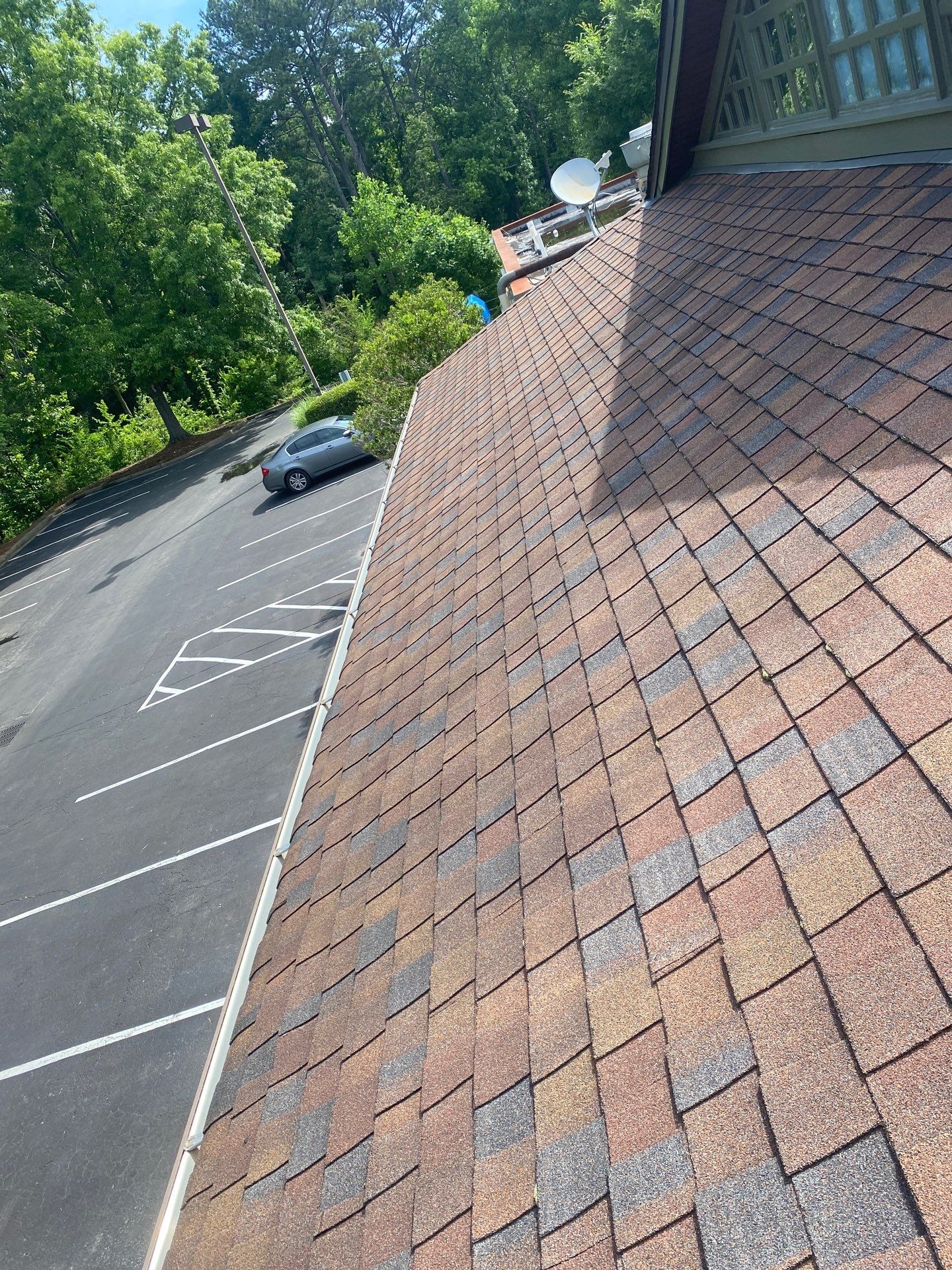 Long commercial gutter run along a shingle roof above a parking area
