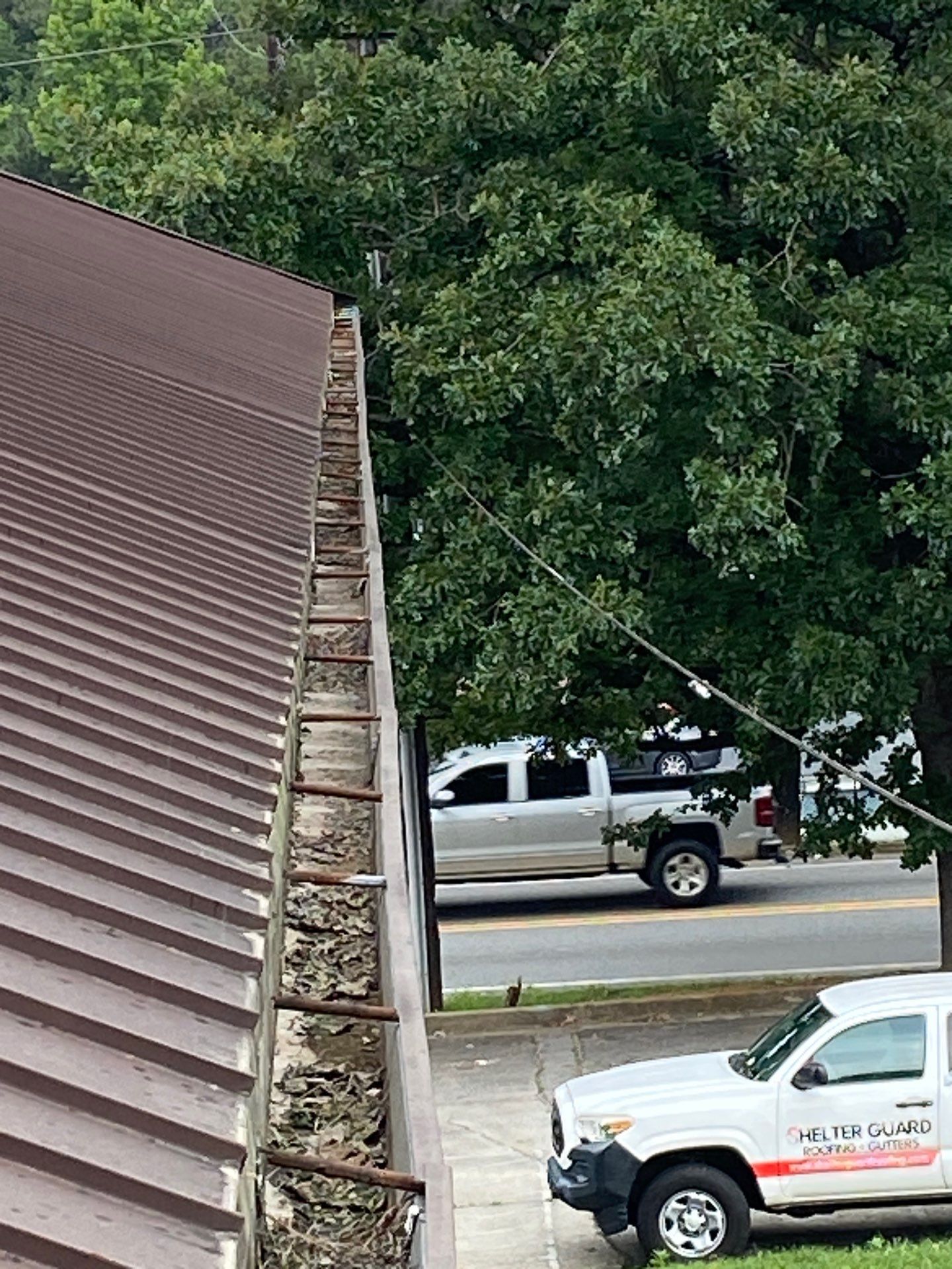 Debris packed along a commercial metal roof gutter with a service truck below
