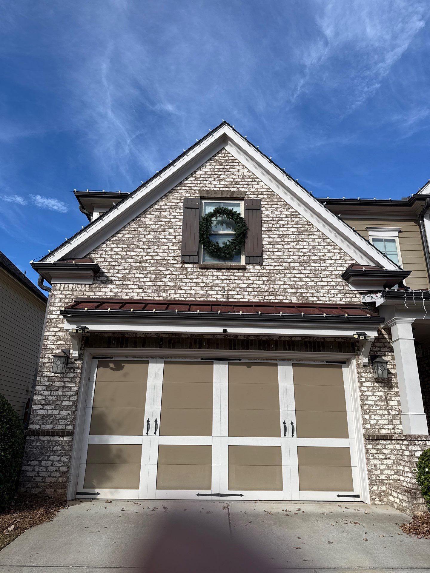 Christmas lights running the roofline of a brick home with a wreath above the garage