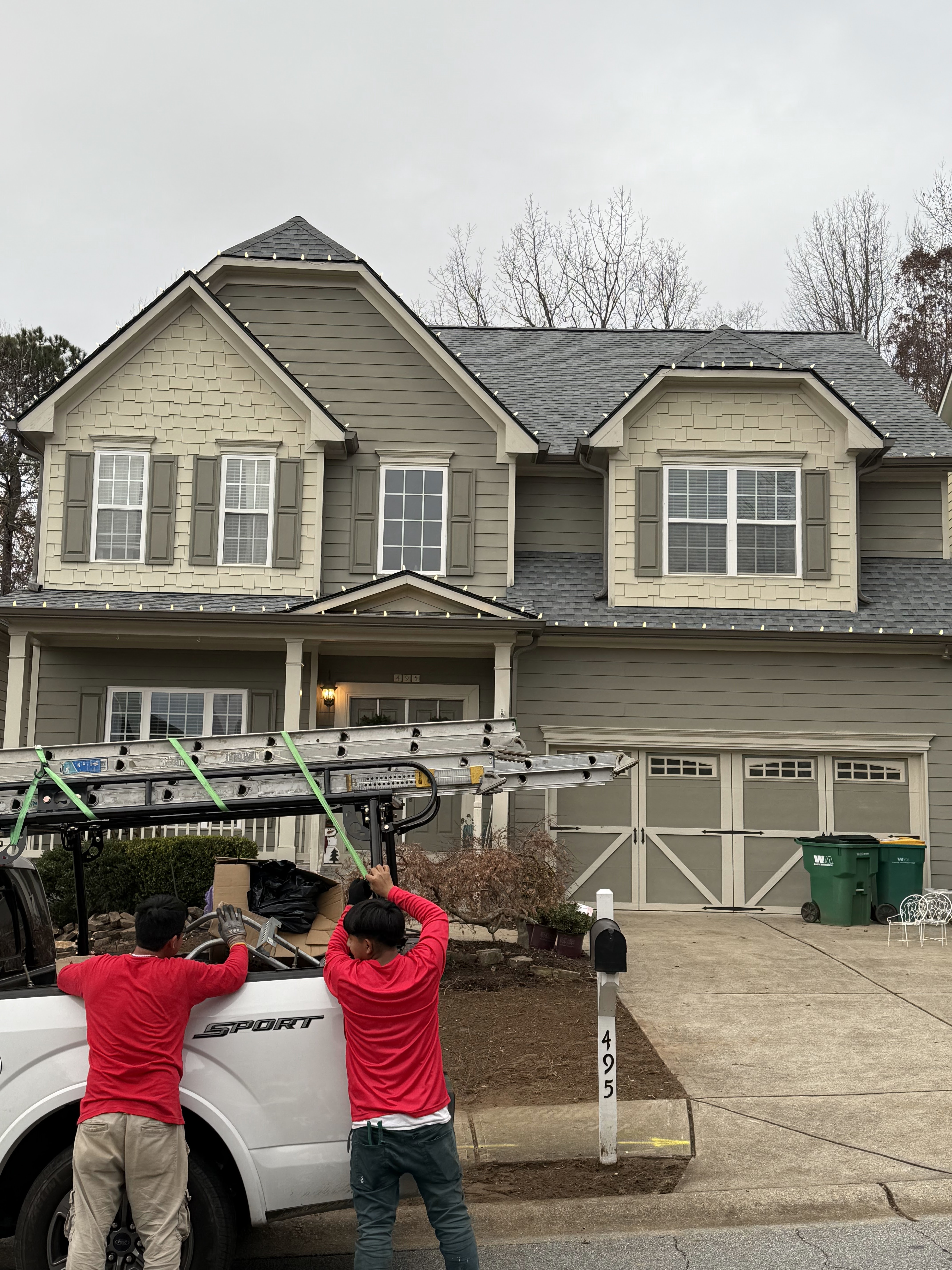 Two crew members loading ladder racks in front of a two-story home before an install