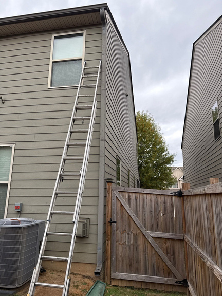 Ladder set against green siding at the downspout of a two-story home