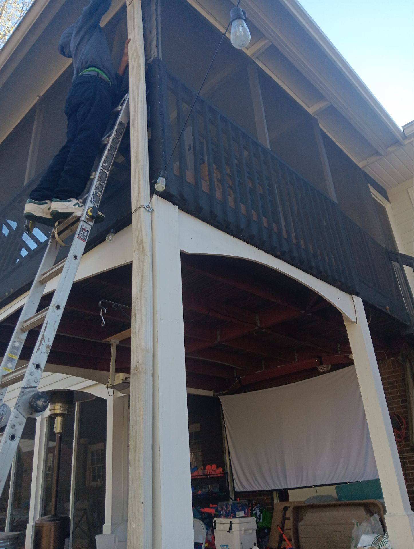 Technician on a ladder working at the downspout of an upper deck