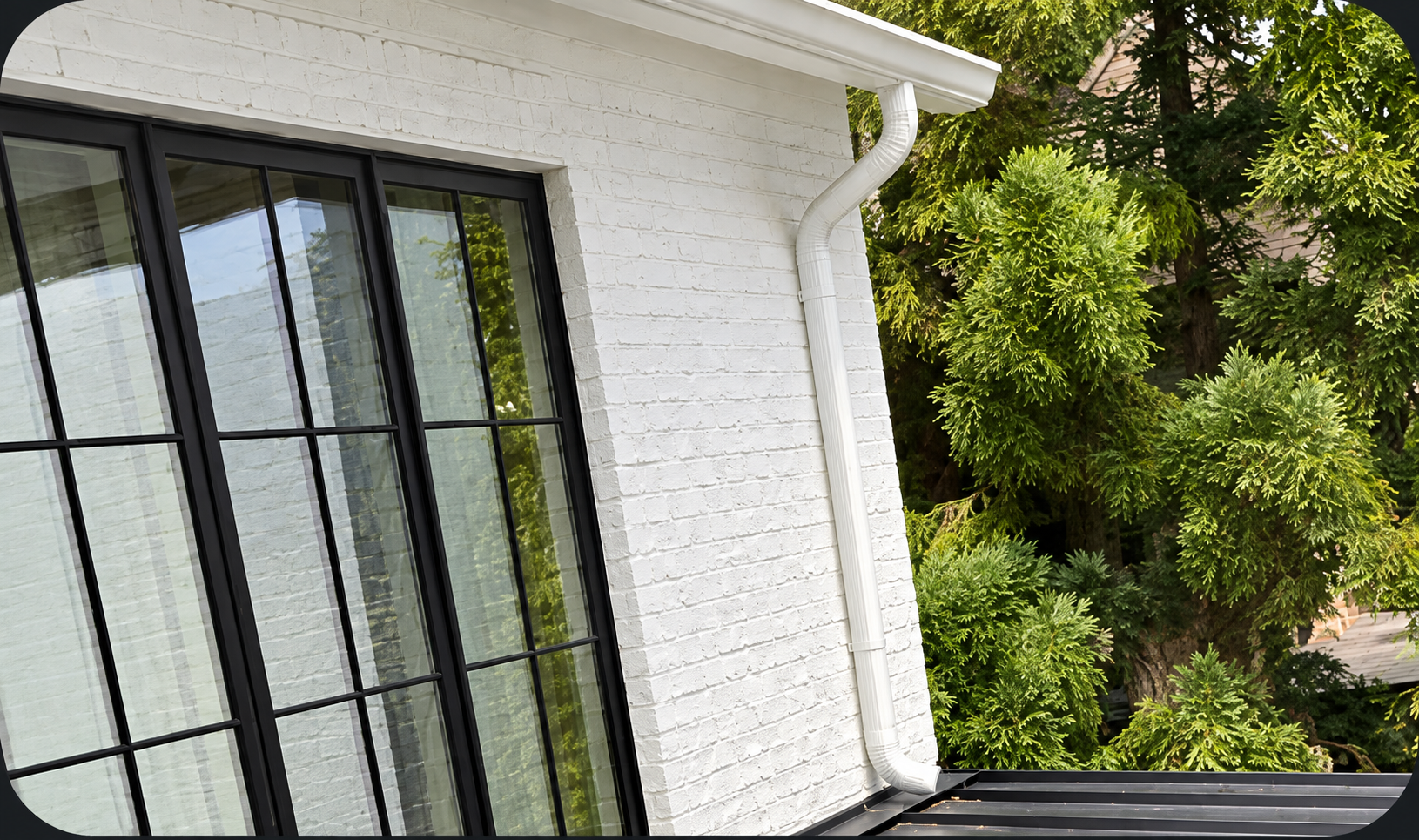 White downspout running down a painted brick wall beside black-framed windows