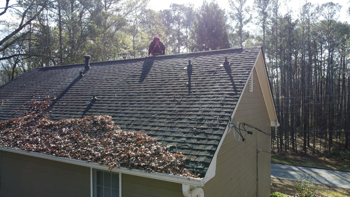Shelter Guard tech on a roof clearing leaves above the gutter line
