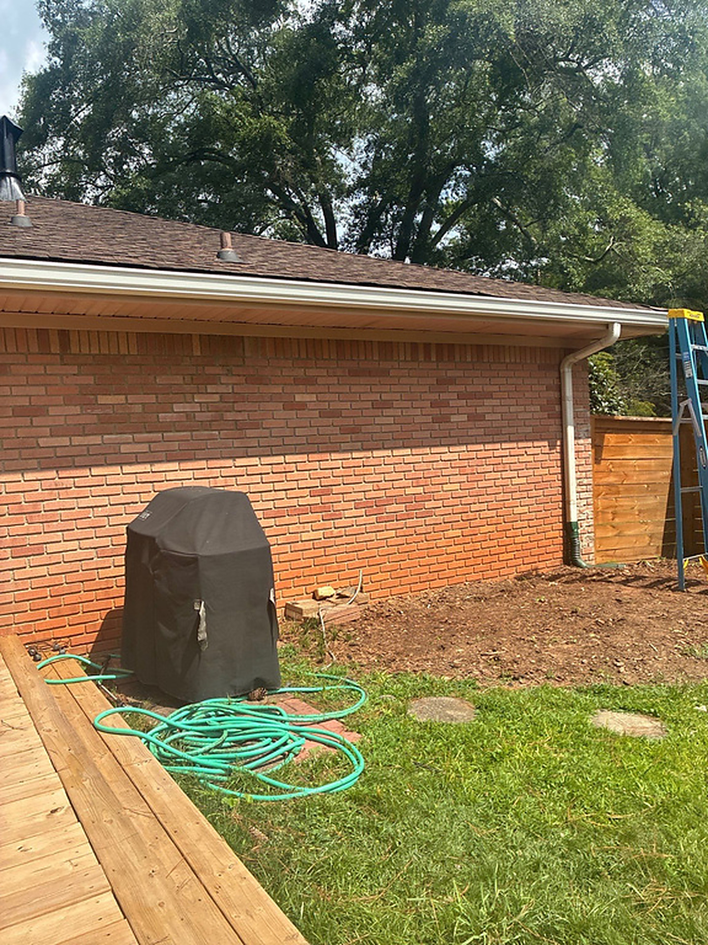 Brick ranch wall with a white downspout running to the yard and a ladder at the fence