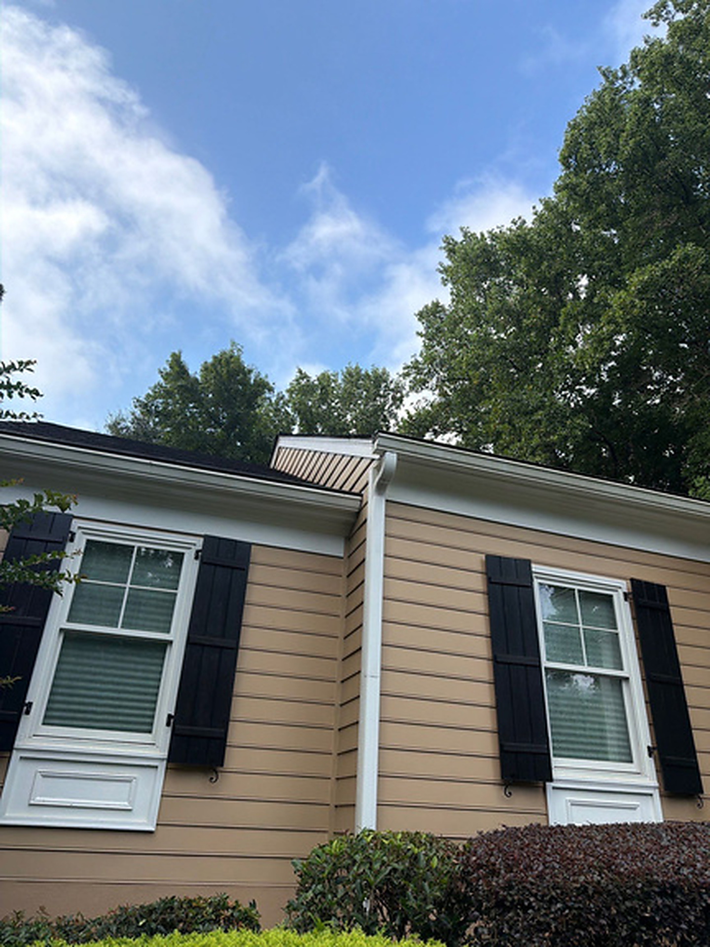 White downspout at the roof corner of a tan siding home with black shutters