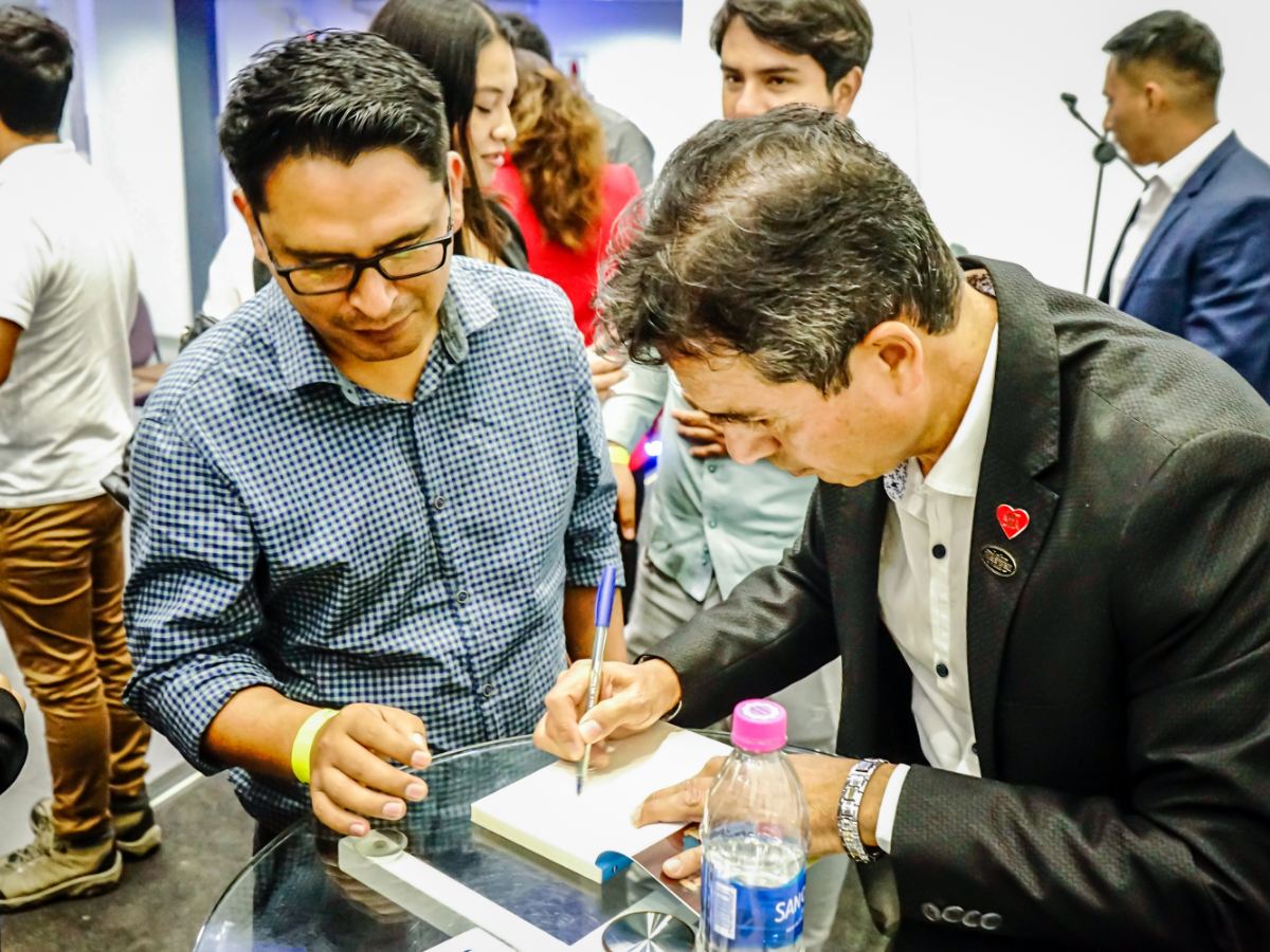 Carlos Calderón firmando libro a asistente en conferencia