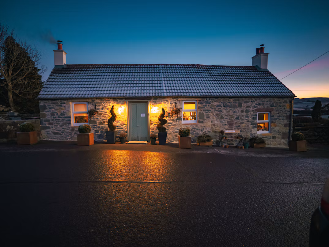 A cosy UK stone cottage with warmly lit windows at dusk