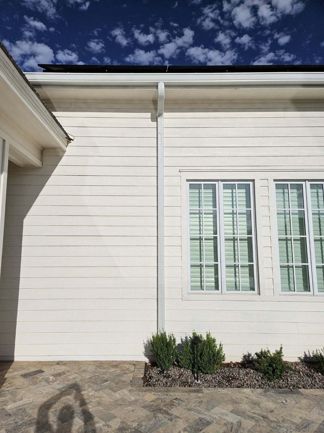 White seamless downspout carrying water down a stucco wall